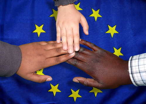Drei Hände mit unterschiedlicher Hautfarbe vor EU-Flagge